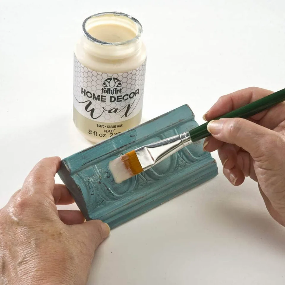 Clear Wax being brushed onto a painted decorative molding. The pictured molding demonstrates application rather than a selected paint color.